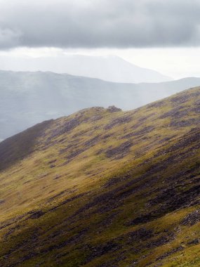 Güneşli dağ sırtı çimenli bir yamaçla parlak bir zemine doğru yol alıyor..