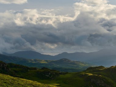 Verimli yeşil bir vadiye bakan kayalık çıkıntılar ve uzak dağlar Ulusal Park 'taki dramatik gri ve beyaz bulutlarla dolu dinamik bir gökyüzü altında..