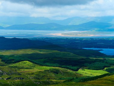 Green hills and forests meet a blue lake.