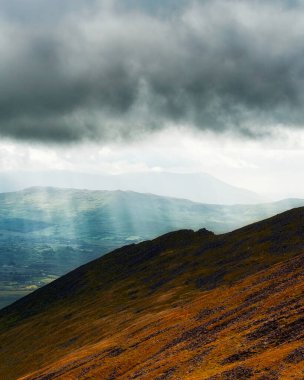Kayalık arazi ve bitki örtüsünün yer aldığı bir dağ sırasının dramatik görüntüsü.