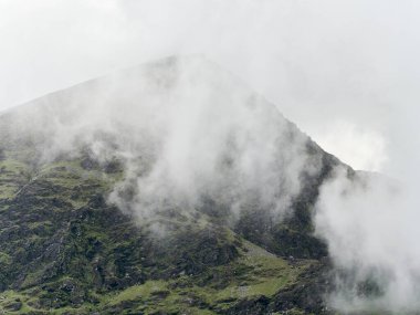 The peak of Carrauntoohil mountain appears through a blanket of thick, white clouds.
