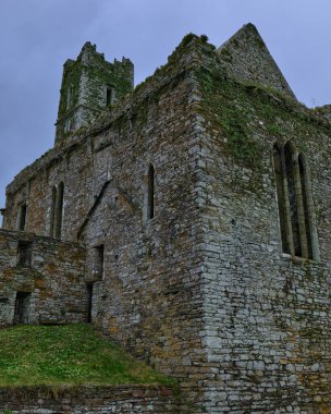 Timoleague, İrlanda, 25 Kasım 2023. Bulutlu gökyüzü İrlanda 'nın County Cork kentindeki Timoleague Abbey' in tarihi kalıntılarının üzerinde beliriyor. Antik taş duvarlar canlı yeşil yosunlarla kaplı..
