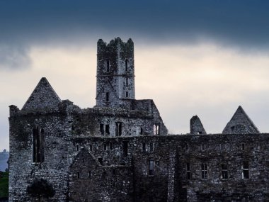 Timoleague, İrlanda, 25 Kasım 2023. Tarihi bir manastırın yıpranmış taş kalıntıları ve yüksek merkezi kulesi dramatik, karanlık bulutlu gökyüzüne karşı duruyor. Antik manastır sitesi.