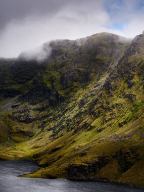 Yeşil yamaçlarla çevrili derin bir vadide dingin bir göl ve dağlardan düşen bir şelale vardır. Dağların tepelerinde bulutlar asılı..