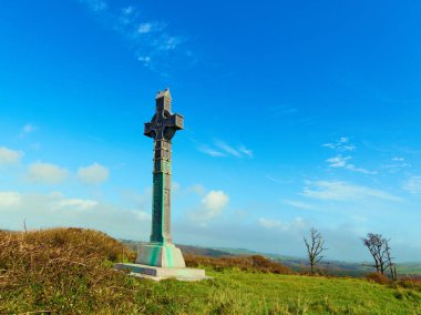 Antik Kelt haçı heykeli engebeli yeşil bir tepede güneşli bir günde engin mavi bir gökyüzünün altında.
