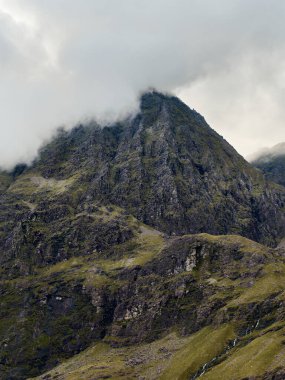 Dik kayalık yamaçlar bulut örtüsüne yükseliyor, jeolojik dokuları yüksek irtifa atmosferiyle harmanlıyor..