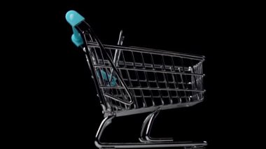 Çok renkli ahşap heykelcikler siyah arka plandaki mini bir alışveriş arabasını dolduruyor. Kara Cuma ve çocukların eğitici oyunları konsepti. Yavaş döndürme