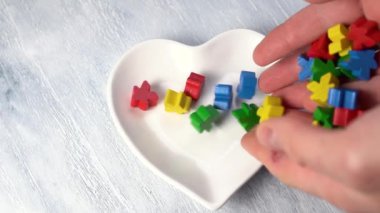 Eller tahtaya kalp şeklinde bir tabağa çok renkli ahşap biblolar döker. Ağır çekim. Döndürme. Sevgililer Günü konsepti