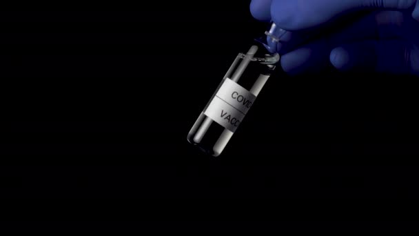 コロナウイルスワクチン試作機Covid 黒の背景に青い医療用手袋の研究者の手の中に近い注射組成のアンプル — ストック動画