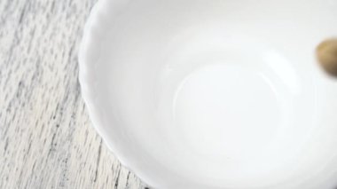 Ahşap desenli arka planda beyaz bir tabağa düşen şam fıstıklarını kapatın. Yavaş çekim