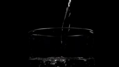 Köpüklü temiz içme suyu akışını kapayarak siyah arka plandaki bir bardağa dökülüyor. Yavaş çekim