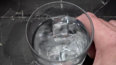 Tahta masada dönen alkollü cam. Buzlu votkayı kapat. İnsan bardağı şeffaf sıvıyla tutar. Eski bir grunge arka planında