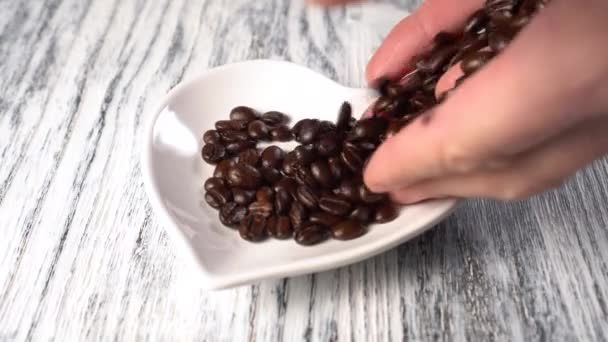Geröstete Kaffeebohnen Werden Von Den Händen Eine Weiße Untertasse Gegossen — Stockvideo