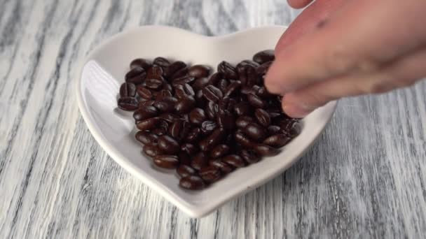 Herzförmige Untertasse Ist Mit Gerösteten Kaffeebohnen Aus Der Hand Gefüllt — Stockvideo