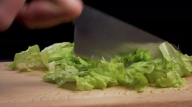 Tahta kesme tahtasının üzerinde taze marul yaprakları kesiyorum. Siyah arka planda yakın plan.