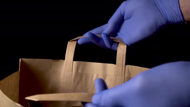 保護医療用手袋の手は オープンペーパーショップバッグを保持します 黒を背景に 安心の考え方 — ストック動画