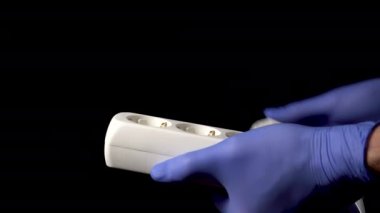 Doktor, tıbbi koruyucu eldivenleri uzatma kablosuna takıyor. Siyah arkaplanı kapat