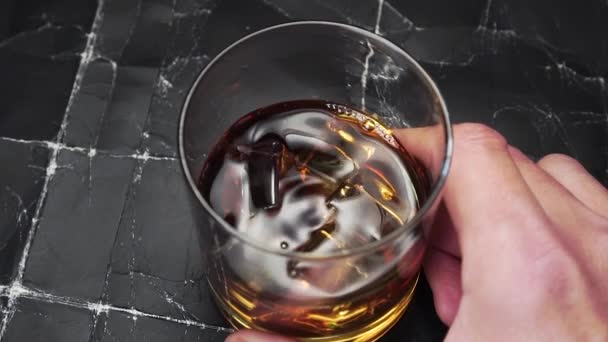 威士忌和冰块在一个玻璃杯中的老式抽象黑色背景 转动手中的杯子 搅拌饮料 靠近点慢动作 — 图库视频影像