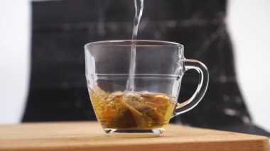 Kaynar su, soyut koyu arkaplanda siyah çay poşeti bulunan şeffaf bir fincana dökülür. Buhar ve sprey. Ahşap bir kesme tahtasının üzerinde güzel kokulu bir içki demlemek. Ağır çekim. Kapat.