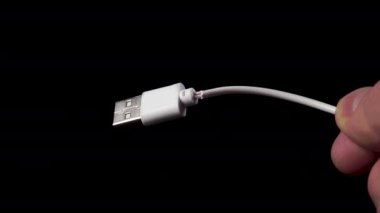 USB priziyle kablo hasar görmüş. Beyaz kırık telefon şarj kablosu elinde. Bozuk elektronik cihaz. Siyah arkaplana yakın plan