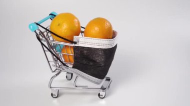 Süpermarket arabasında, tek kullanımlık tıbbi maske takan olgun mandalinalar. Minyatür. Güvenli alışveriş konsepti