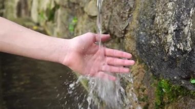 Çocuk, doğal, eski bir taş pınarında su sıçratarak maden dağı suyuna dokunuyor. Duvarlarda yosun var. Kapatın. Yavaş çekim