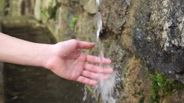 Doğal bir dağ pınarından gelen ferahlatıcı temiz su akıntısı genç bir eli sulandırır. Yosun kaplı ıslak taşlar. Kapatın. Yavaş çekim