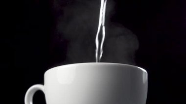 Kaynar su siyah arka planda beyaz bir kahve bardağına dökülür. Buhar yakın planda buharlaşır. Ağır çekim. Makro çekim