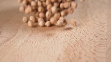 Bir grup nohut beyaz bir seramik bardaktan kesme tahtasının ahşap yüzeyine dökülür. Sağlıklı gıda konsepti. Yavaş çekim