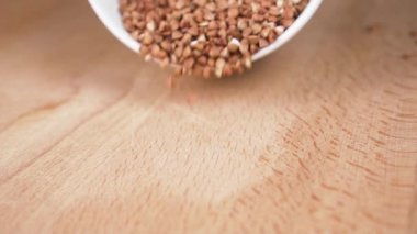 Beyaz bir kaseden fırında pişmemiş karabuğday. Ağır çekimde düşüyorum. Yakın plan. Sağlıklı gıda konsepti