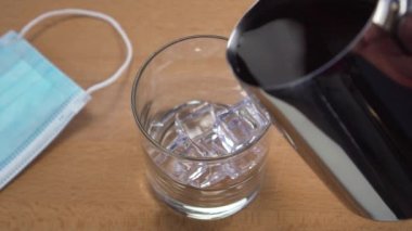 Kafeteryadaki buzlu bir bardağa buzlu çay dolduruyorum. Tahta bir masada, tıbbi koruyucu bir maskeyle. Virüs ve karantinayla ilgili yeni gerçeklik kavramı. Koronavirüs kilitlenmesi fikri.