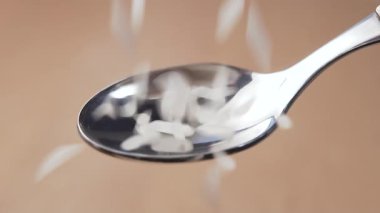 Beyaz, uzun pirinçler arka plandaki metal bir kaşığa dökülüyor. Makro. Yavaş çekim