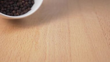 Karabiber çeşnisi beyaz bir seramik kaseden ahşap bir yüzeye düşer. Ağır çekim. Yakın plan. Baharatlı baharat.