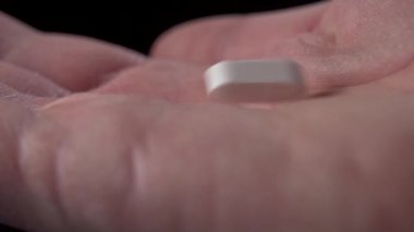 Hapın makro aşısı yavaş çekimde avuç içine düşer. El ilaç almak için hap alır. Kapatın. Siyah arkaplan