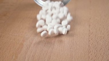 Tıbbi beyaz haplar, yavaş çekimde cam şeffaf bir kabın üzerine serpiştirilir.