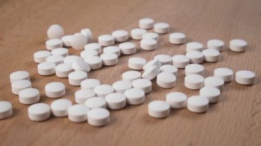 Beyaz haplar ağır çekimde ahşap bir masaya saçılıyor. Kapatın. Sağlık kavramı