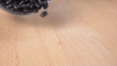 Ağır çekimde siyah fasulye, beyaz kaseden ahşap masaya düşüyor.