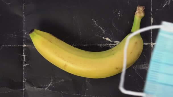 一个医疗面罩掉在一个成熟的香蕉上 上面是一个皱皱的黑色旧背景 慢动作避孕和受保护的性概念 — 图库视频影像