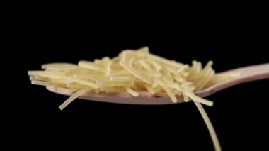 Ahşap bir kaşık dolusu pişmemiş kırık spagetti. Ağır çekimde çiğ vermicelli dökülüyor. Siyah arkaplanda makro