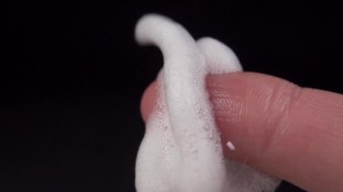 Siyah arka planda beyaz köpük yavaş çekimde parmağa düşer. Makro atış. Hijyenik cilt bakımı kavramı