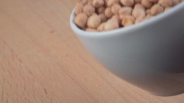 Düşen nohutlar, beyaz bir kasenin kesme tahtasına yakın çekimde düşerler.