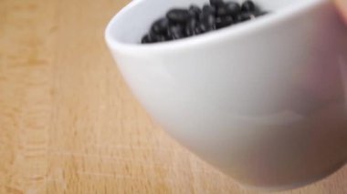 Siyah fasulyeler beyaz bir bardaktan yavaşça tahtaya fırlatılır.
