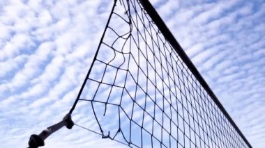 Parlak sirrus bulutlarının arkaplanına karşı voleybol ağı yırtıldı. Terk edilmiş bir spor sahasında düğümlenmiş bir iple gerilmiş ağ siluetleri.