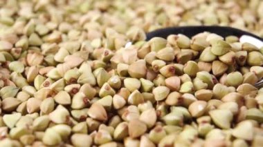 Bir kaşık, çiğ yeşil karabuğday tanelerini yakından yakalar. Makro atış. Döndürme. Biyolojik ürün