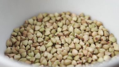 ?Beyaz bir kâseyi dolduran pişmemiş yeşil karabuğday tanelerinden kurtul. Yavaş çekim