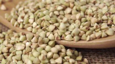 Karabuğday, ağır çekimde çuval bezi üzerinde tahta bir kaşığa düşer. Pişmemiş bir yığın yeşil karabuğday. Makro çekim