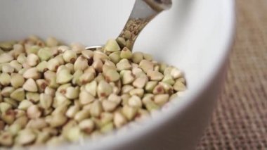 Metal kaşık, çiğ yeşil karabuğdayı beyaz bir kasede yavaş çekimde karıştırır. Makro atış. Sağlıklı kahvaltı kavramı