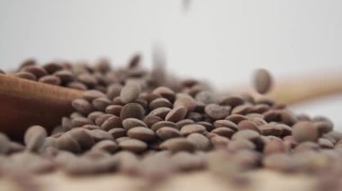 Çiğ kahverengi mercimek, yakın plan tahta kaşığa düşer. Ağır çekim. Makro atış. Seçici odak