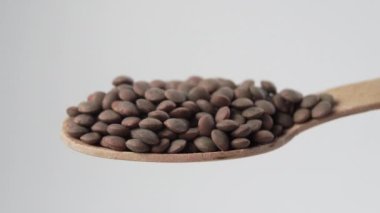 Ahşap kaşık dolusu pişmemiş çiğ mercimek. Yavaş çekimde düşen mercimek fasulyesi. Makro çekim