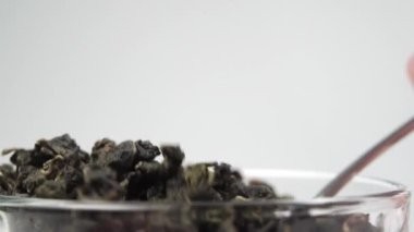 Çay kaşığındaki inciler şeklinde sarılmış yeşil kaliteli çay yaprakları. Barut çay topları yavaş çekimde beyaz arka planda cam bir fincana düşüyor. Makro çekim
